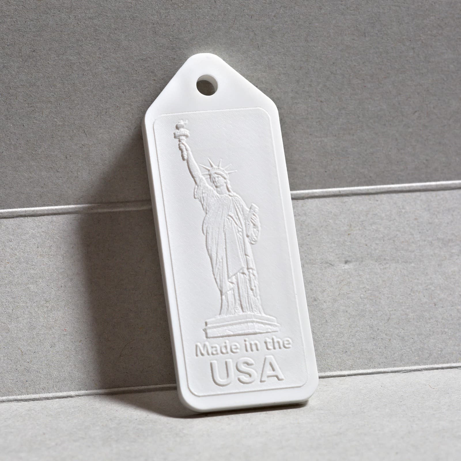 A finished white molded keychain with fine embossed detail